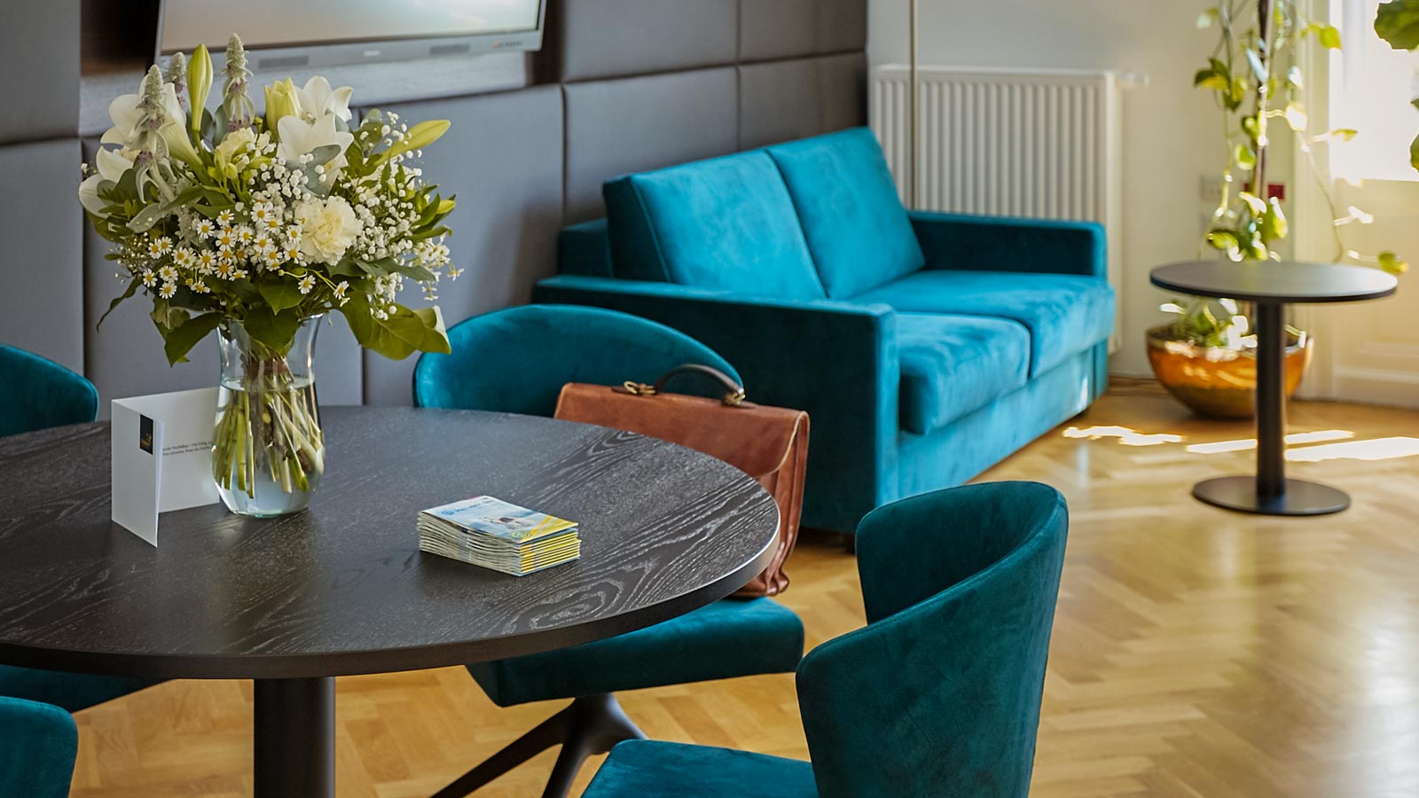 Elegante Lobby mit Blumenstrau&szlig; auf Tisch, blauen M&ouml;beln und Pflanzen im Hintergrund.